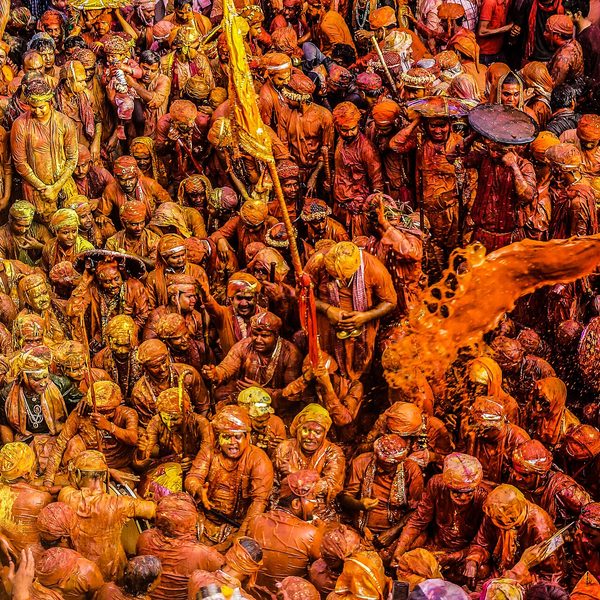 A vast crowd covered in yellow and orange colour, celebrating Holi in Mathura